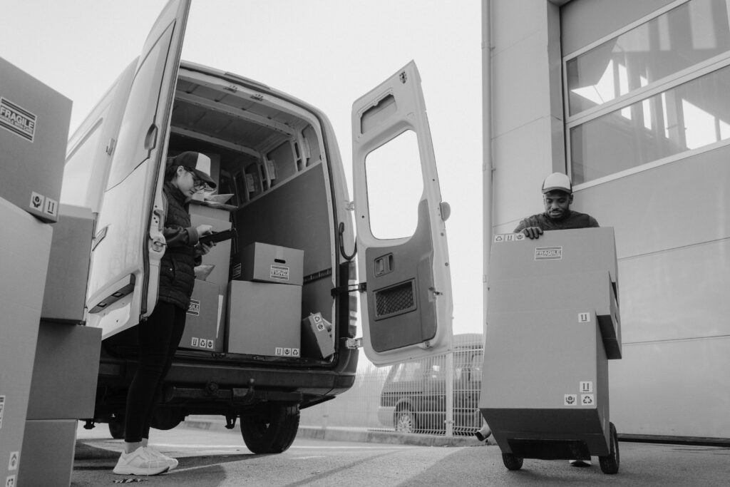 Delivery workers unloading packages from a van using a trolley at a distribution center.